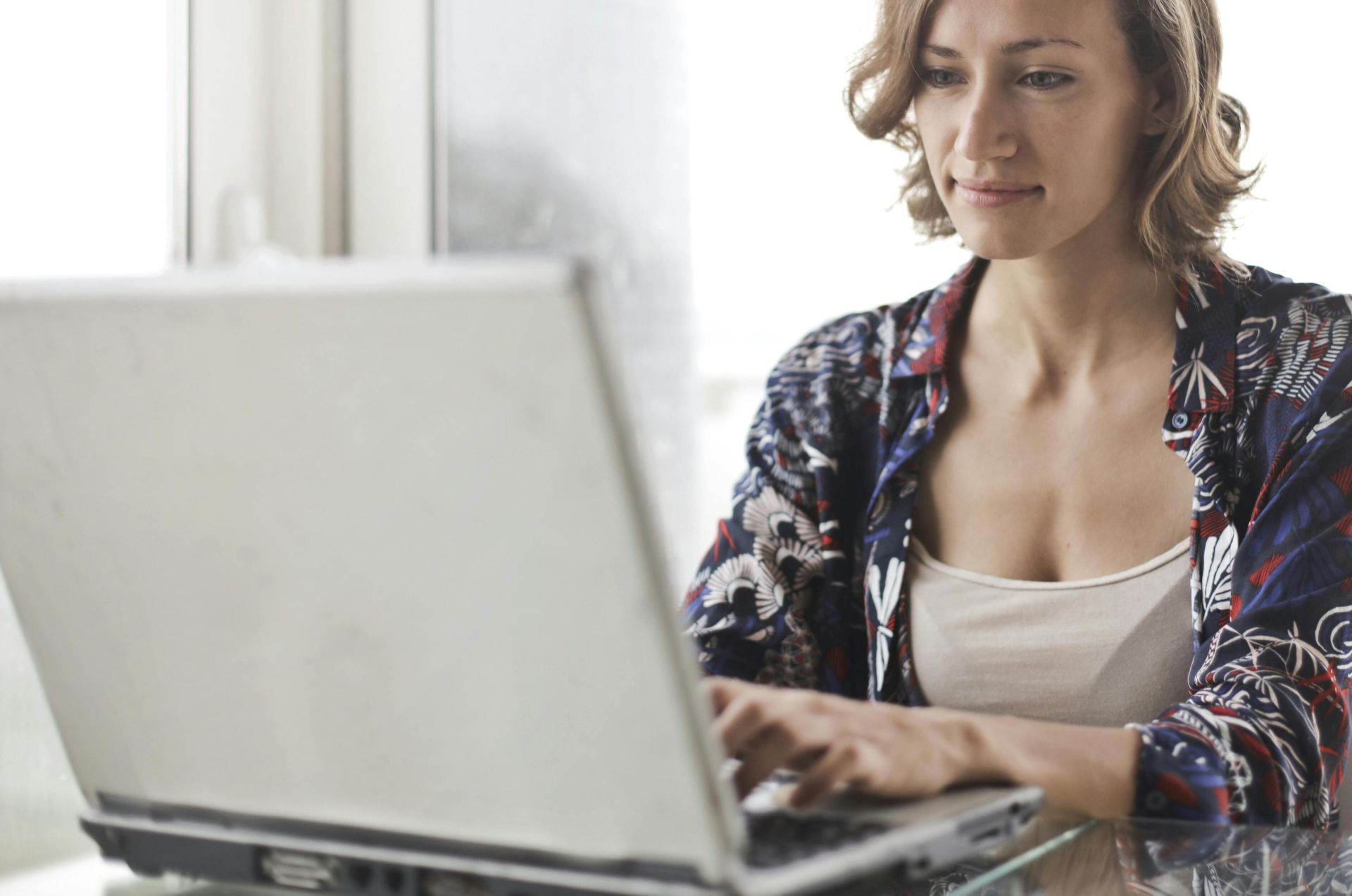 A woman typing on a laptop in a bright, modern home office setting.